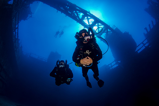 A SCR diver explorer the cargo holds of the Spiegel Grove silhouetted with the cranes and the superstructure oin the background, Florida Keys, Atlantic Ocean.
